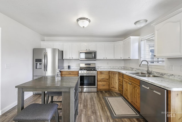 kitchen with a sink, light countertops, appliances with stainless steel finishes, dark wood-style floors, and white cabinetry