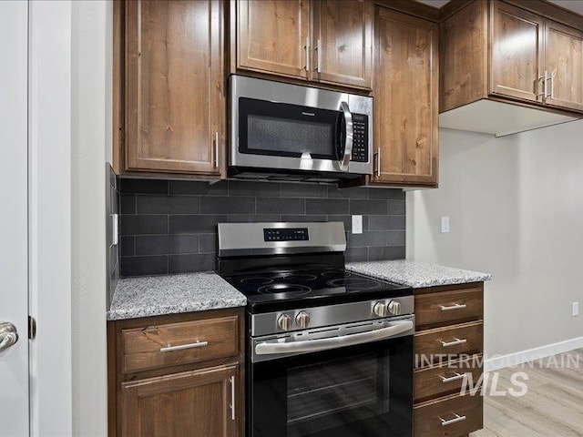 kitchen with baseboards, light stone countertops, stainless steel appliances, light wood-style floors, and backsplash