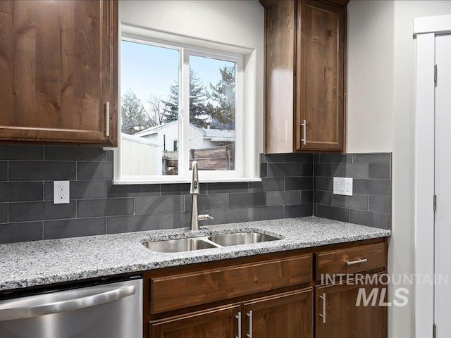 kitchen with stainless steel dishwasher, light stone counters, backsplash, and a sink