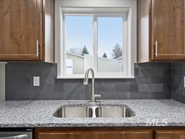 kitchen featuring light stone counters, brown cabinetry, and a sink