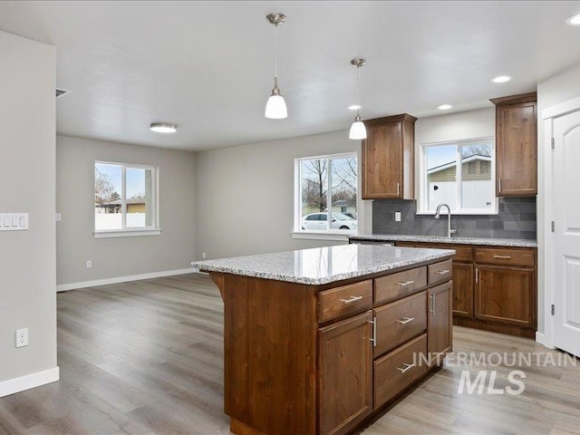 kitchen with light stone counters, tasteful backsplash, hanging light fixtures, a kitchen island, and wood finished floors