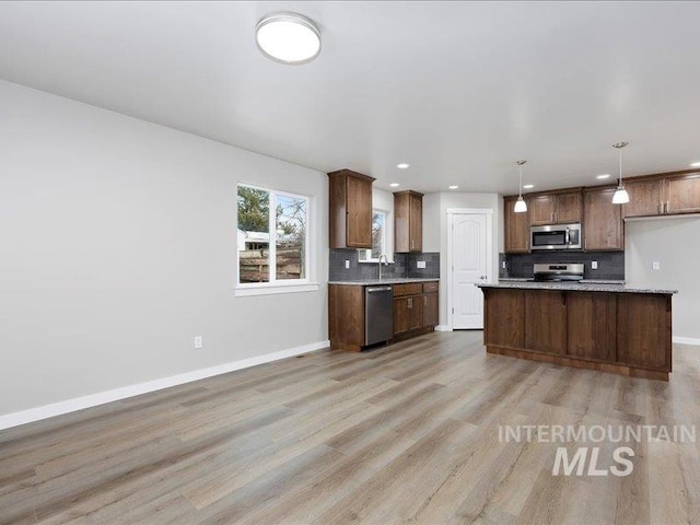 kitchen with appliances with stainless steel finishes, brown cabinetry, light countertops, and hanging light fixtures