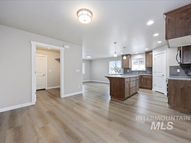 kitchen with light wood-style floors, a center island, decorative light fixtures, and backsplash