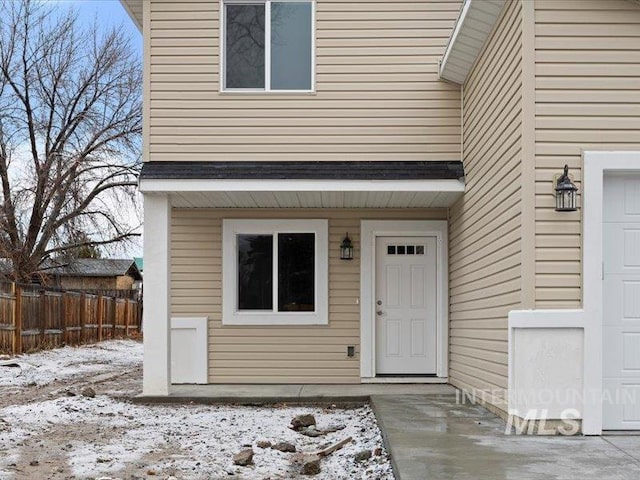 snow covered property entrance featuring a garage and fence