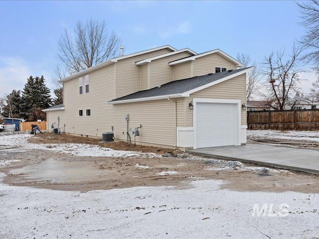 snow covered property with an attached garage, fence, cooling unit, and concrete driveway