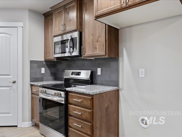 kitchen with light wood finished floors, light stone counters, stainless steel appliances, and backsplash