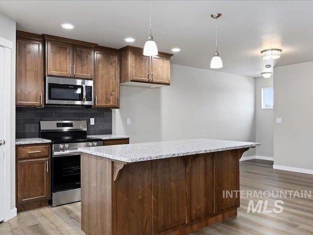 kitchen featuring stainless steel appliances, hanging light fixtures, light wood-type flooring, backsplash, and a center island