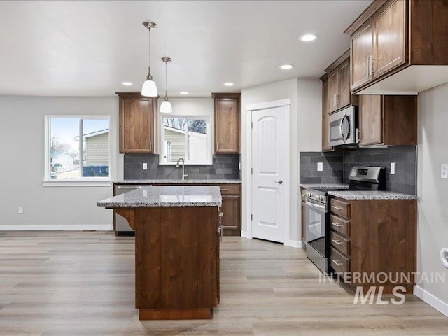 kitchen featuring baseboards, a kitchen island, appliances with stainless steel finishes, light stone counters, and pendant lighting