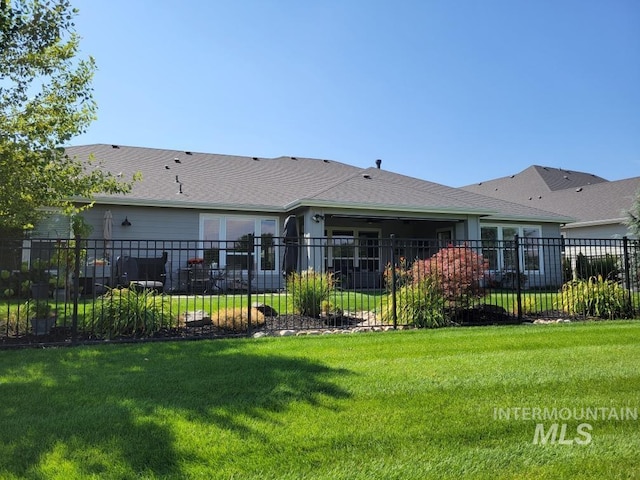 rear view of property with a yard, fence, and a shingled roof