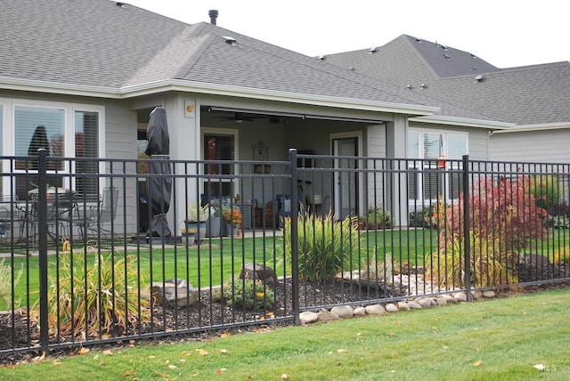 rear view of house with a lawn, roof with shingles, and fence