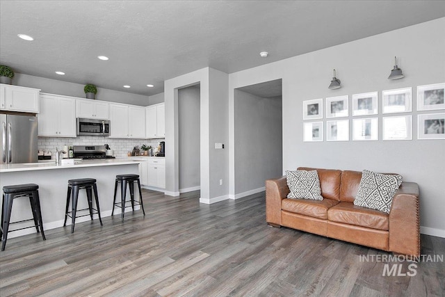 living area featuring a textured ceiling, recessed lighting, wood finished floors, and baseboards