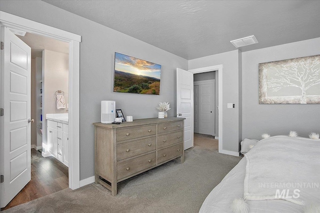 carpeted bedroom with a textured ceiling, connected bathroom, visible vents, and baseboards