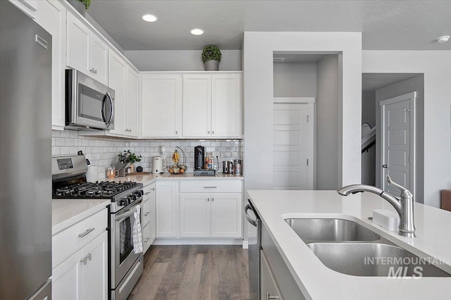 kitchen featuring white cabinets, appliances with stainless steel finishes, dark wood-style flooring, a sink, and backsplash