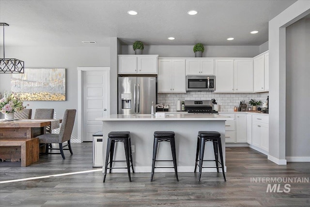 kitchen with a breakfast bar area, dark wood-style flooring, a kitchen island with sink, stainless steel appliances, and backsplash