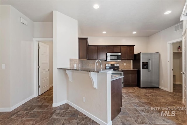 kitchen featuring visible vents, a breakfast bar area, stainless steel appliances, and decorative backsplash