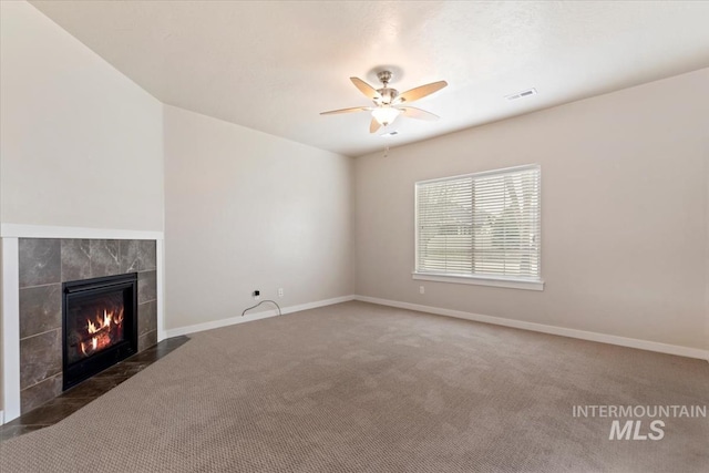 unfurnished living room featuring visible vents, a tiled fireplace, carpet floors, baseboards, and ceiling fan