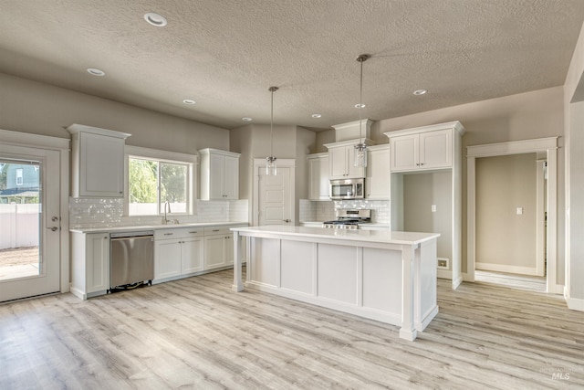 kitchen with light hardwood / wood-style floors, white cabinets, a kitchen island, stainless steel appliances, and decorative light fixtures