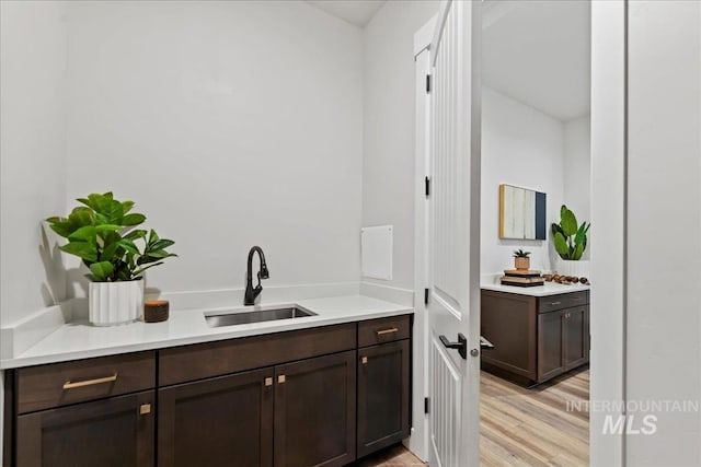 bar featuring dark brown cabinetry, sink, and light wood-type flooring