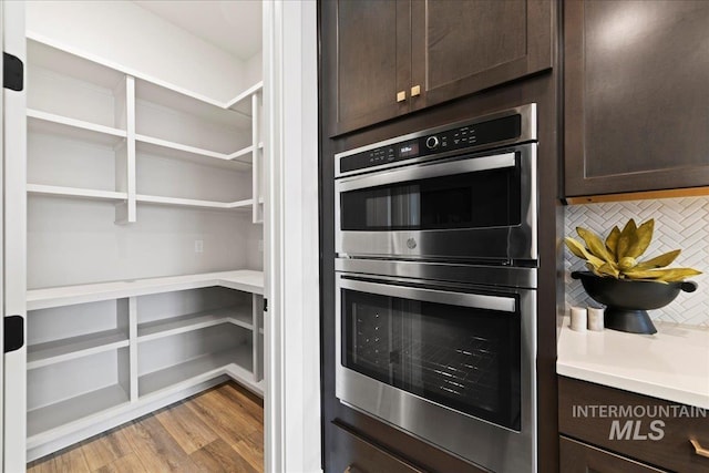 kitchen featuring decorative backsplash, dark brown cabinets, stainless steel double oven, and light wood-type flooring