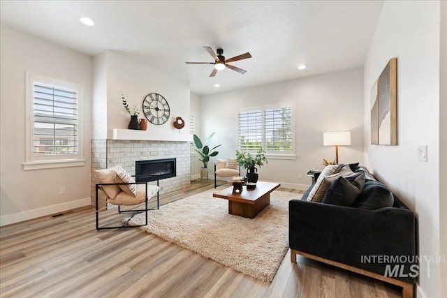 living room featuring hardwood / wood-style flooring, ceiling fan, and a brick fireplace