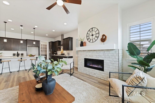 living room featuring ceiling fan, light hardwood / wood-style floors, and a brick fireplace