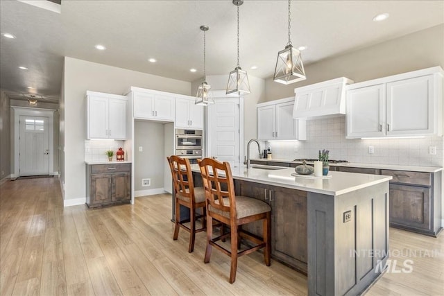 kitchen featuring light wood finished floors, white cabinets, appliances with stainless steel finishes, custom exhaust hood, and a sink