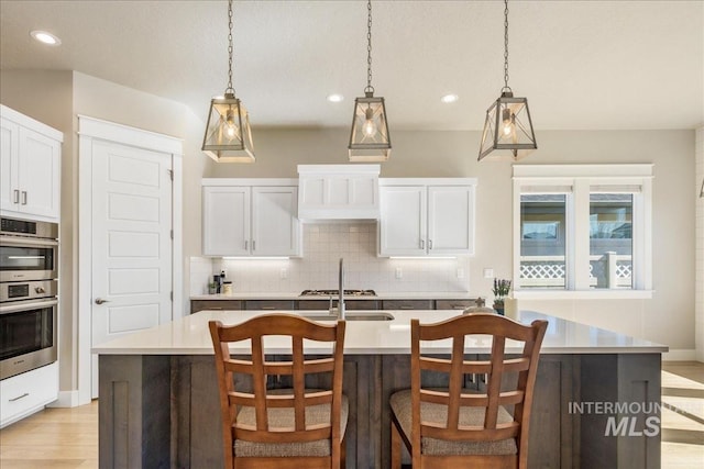 kitchen featuring tasteful backsplash, a center island with sink, white cabinetry, and light countertops