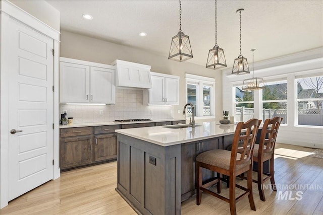 kitchen featuring custom exhaust hood, light wood finished floors, tasteful backsplash, light countertops, and a sink