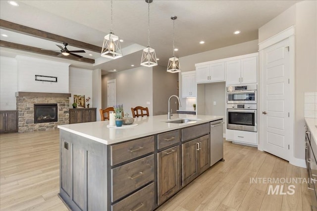 kitchen with stainless steel appliances, light countertops, light wood-style floors, white cabinetry, and a sink