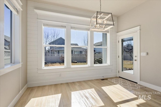 unfurnished dining area featuring an inviting chandelier, visible vents, baseboards, and wood finished floors