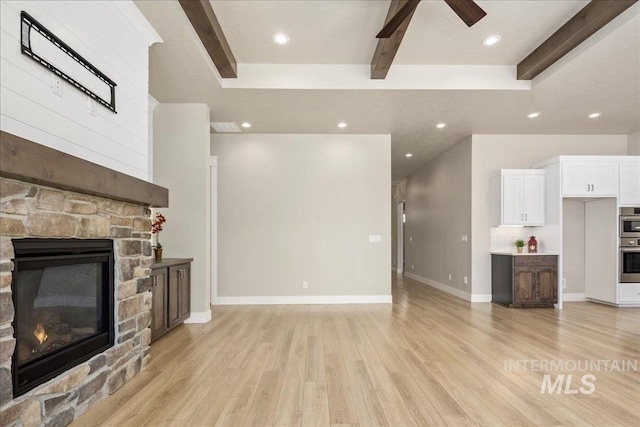 unfurnished living room with light wood finished floors, baseboards, a ceiling fan, a stone fireplace, and beam ceiling