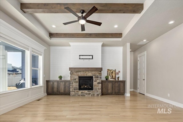 living area featuring light wood-type flooring, baseboards, beamed ceiling, and a stone fireplace