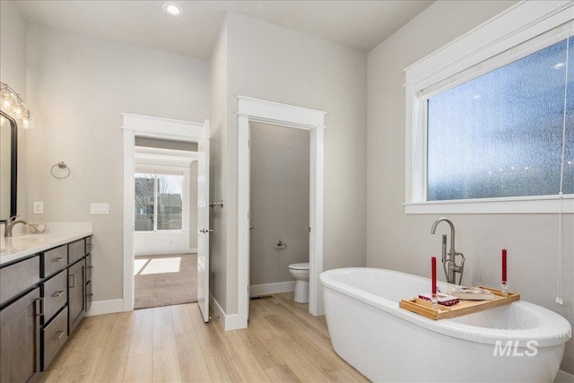 bathroom featuring toilet, wood finished floors, vanity, baseboards, and a freestanding bath