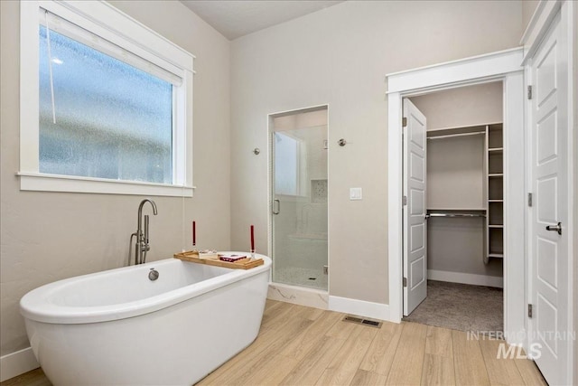 bathroom with a soaking tub, visible vents, a spacious closet, a stall shower, and wood finished floors