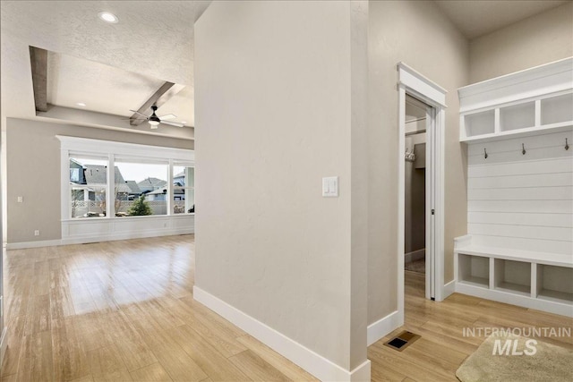 hallway with visible vents, a textured ceiling, baseboards, and wood finished floors