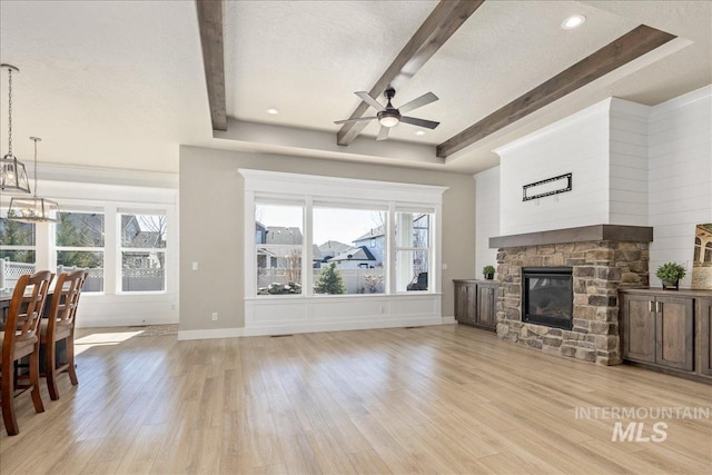 living area featuring light wood-type flooring, plenty of natural light, beam ceiling, and a stone fireplace