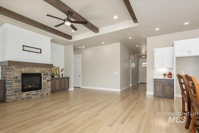 living room with light wood-type flooring, baseboards, beam ceiling, and a stone fireplace