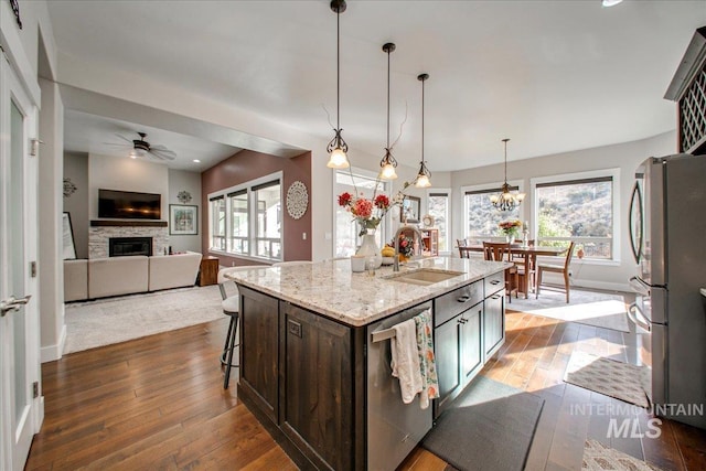 kitchen featuring light stone counters, an island with sink, appliances with stainless steel finishes, pendant lighting, and sink