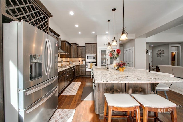 kitchen with a large island with sink, wood-type flooring, sink, stainless steel appliances, and decorative backsplash