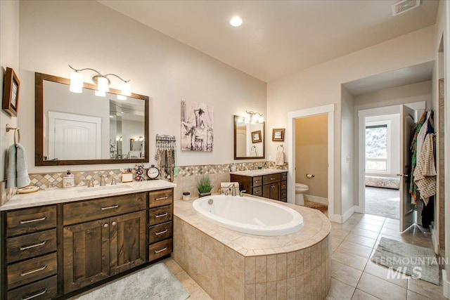 bathroom featuring toilet, vanity, tile patterned floors, and tiled bath