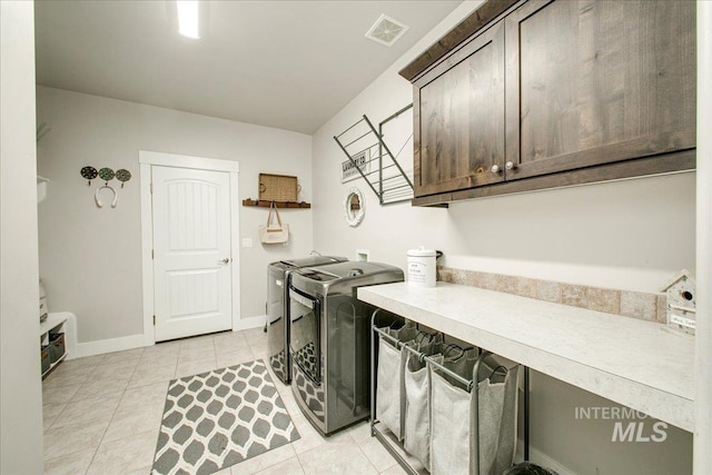 laundry area with washing machine and dryer, light tile patterned floors, and cabinets