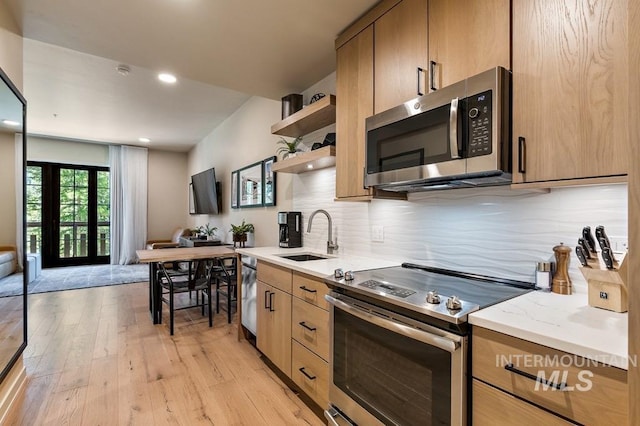 kitchen featuring light wood finished floors, decorative backsplash, stainless steel appliances, open shelves, and a sink