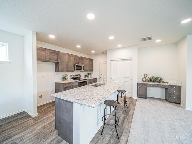 kitchen with sink, hardwood / wood-style flooring, a breakfast bar, appliances with stainless steel finishes, and an island with sink