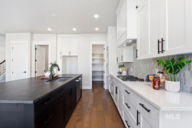 kitchen featuring custom exhaust hood, white cabinets, an island with sink, dark wood-type flooring, and sink