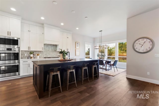 kitchen featuring decorative backsplash, dark hardwood / wood-style flooring, a breakfast bar, white cabinetry, and a kitchen island with sink