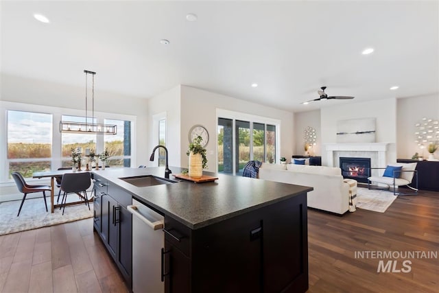 kitchen featuring an island with sink, dark hardwood / wood-style floors, dishwasher, decorative light fixtures, and sink