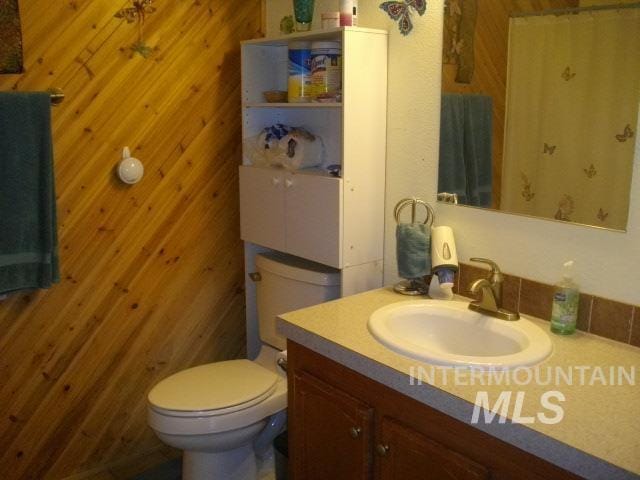 bathroom with toilet, vanity, and wood walls