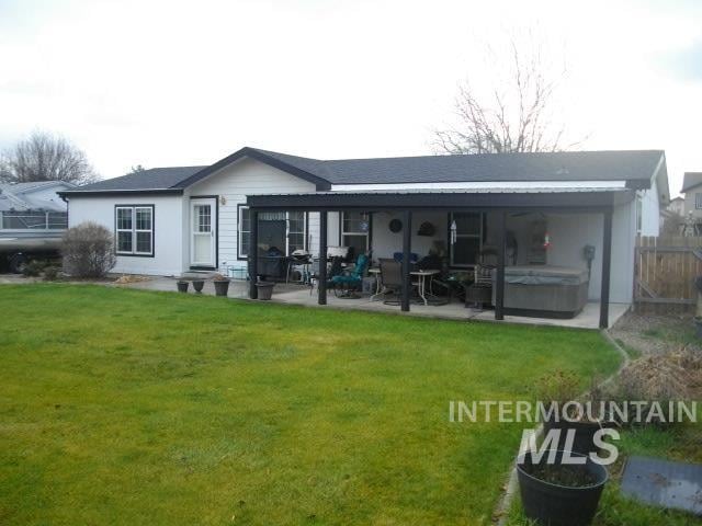 rear view of property featuring a lawn, a patio area, and a hot tub