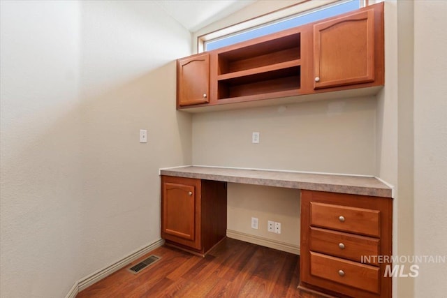 unfurnished office with dark wood-style floors, visible vents, built in desk, and baseboards