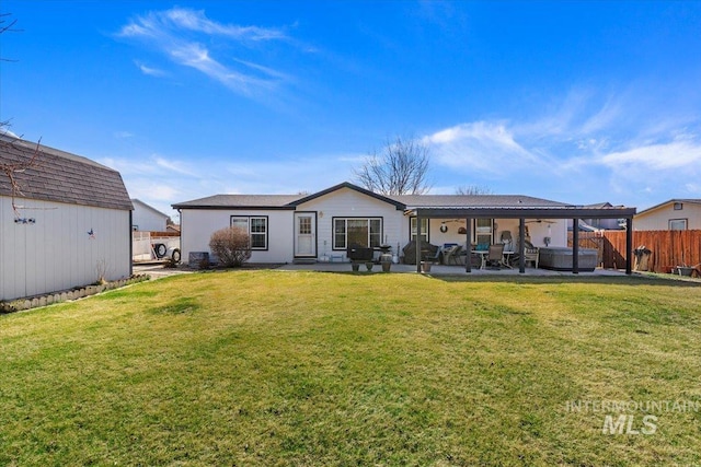 rear view of house with a hot tub, fence, a lawn, an outdoor structure, and a patio area